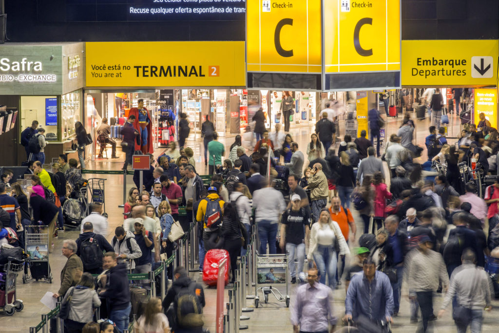Aeroporto: multidão em movimento, balcões de check-in e sinalização para embarques.