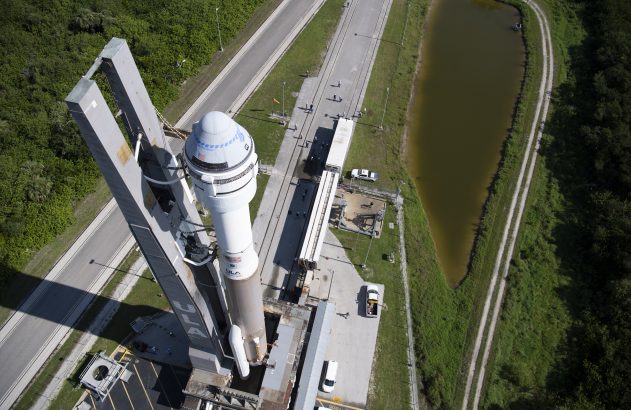 Vista aérea de um foguete Atlas V com Starliner na plataforma de lançamento, cercado por estradas, lago e vegetação.