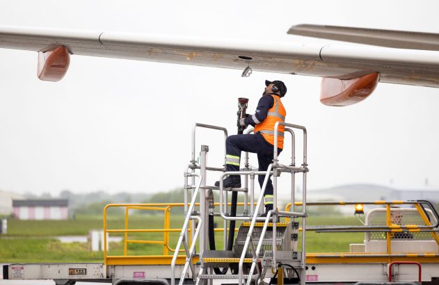 Trabalhador em plataforma elevatória reabastecendo asa de avião em um aeroporto.