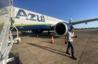 Funcionário da Azul caminha no pátio, próximo a avião da Azul com escada de embarque.