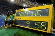 Usain Bolt agachado, apontando, ao lado de placar eletrônico amarelo exibindo "NEW WR" e "9.58". Estádio ao fundo.