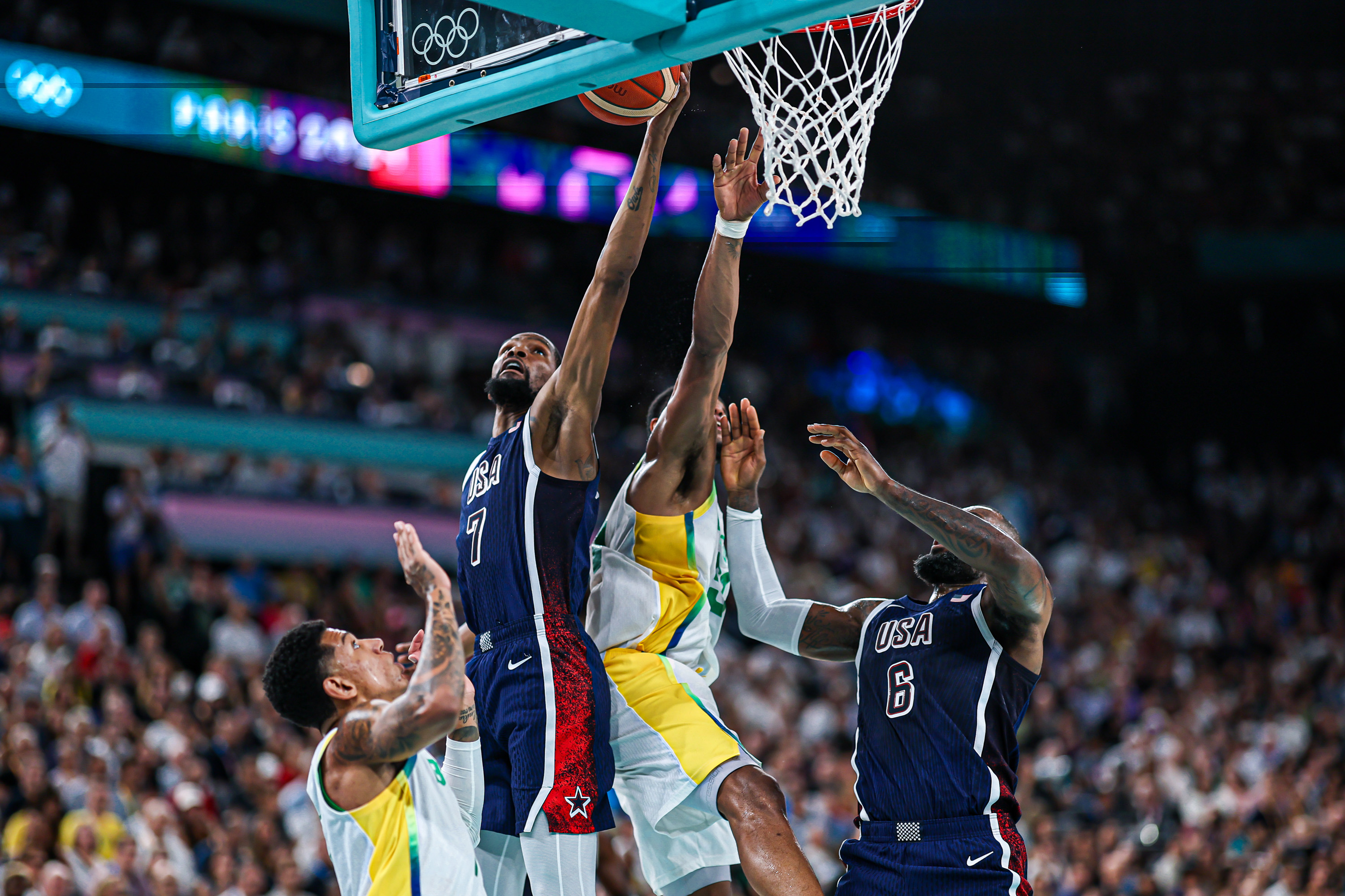 Kevin Durant (EUA, nº 7) arremessa bola na cesta. LeBron James (nº 6) e oponentes em quadra de basquete.