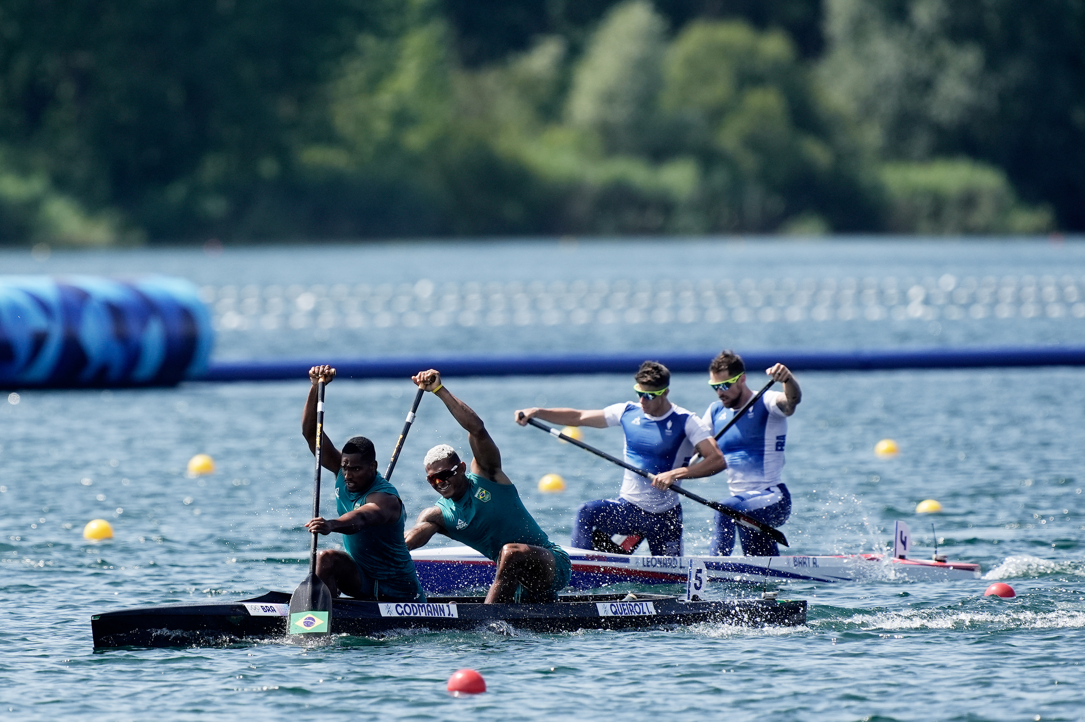 Corrida de canoagem. Dois remadores brasileiros à frente de dois franceses em águas calmas e ensolaradas.