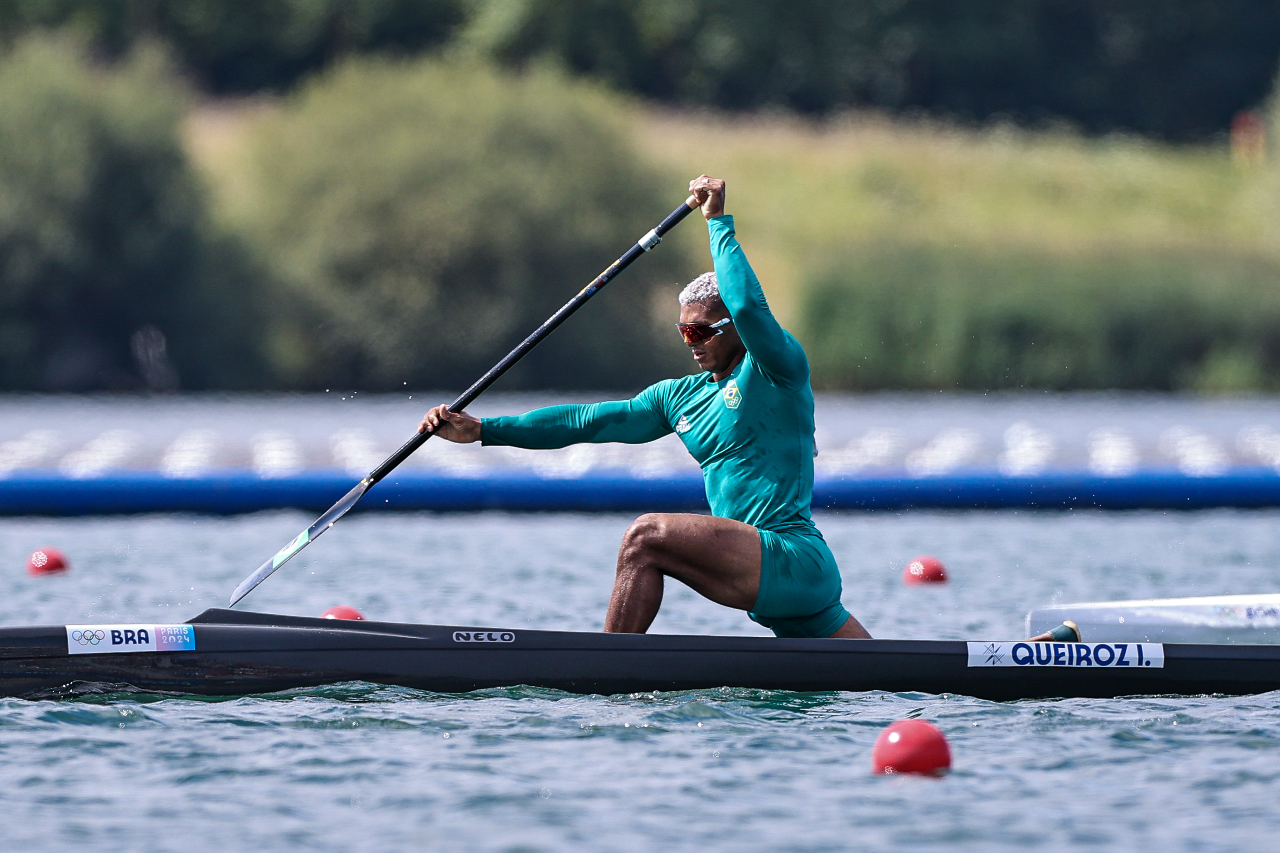 Atleta com roupa turquesa remando em canoa preta numa corrida aquática.
