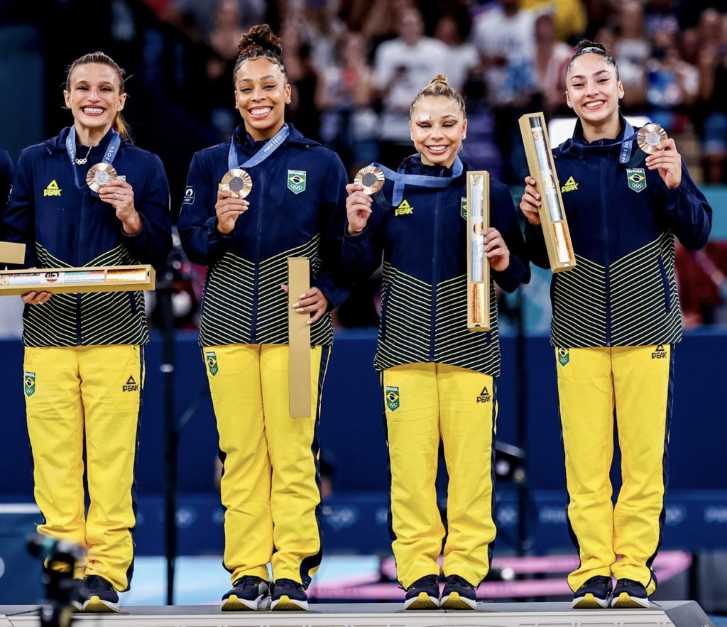 Time feminino brasileiro com medalhas e prêmios no pódio.