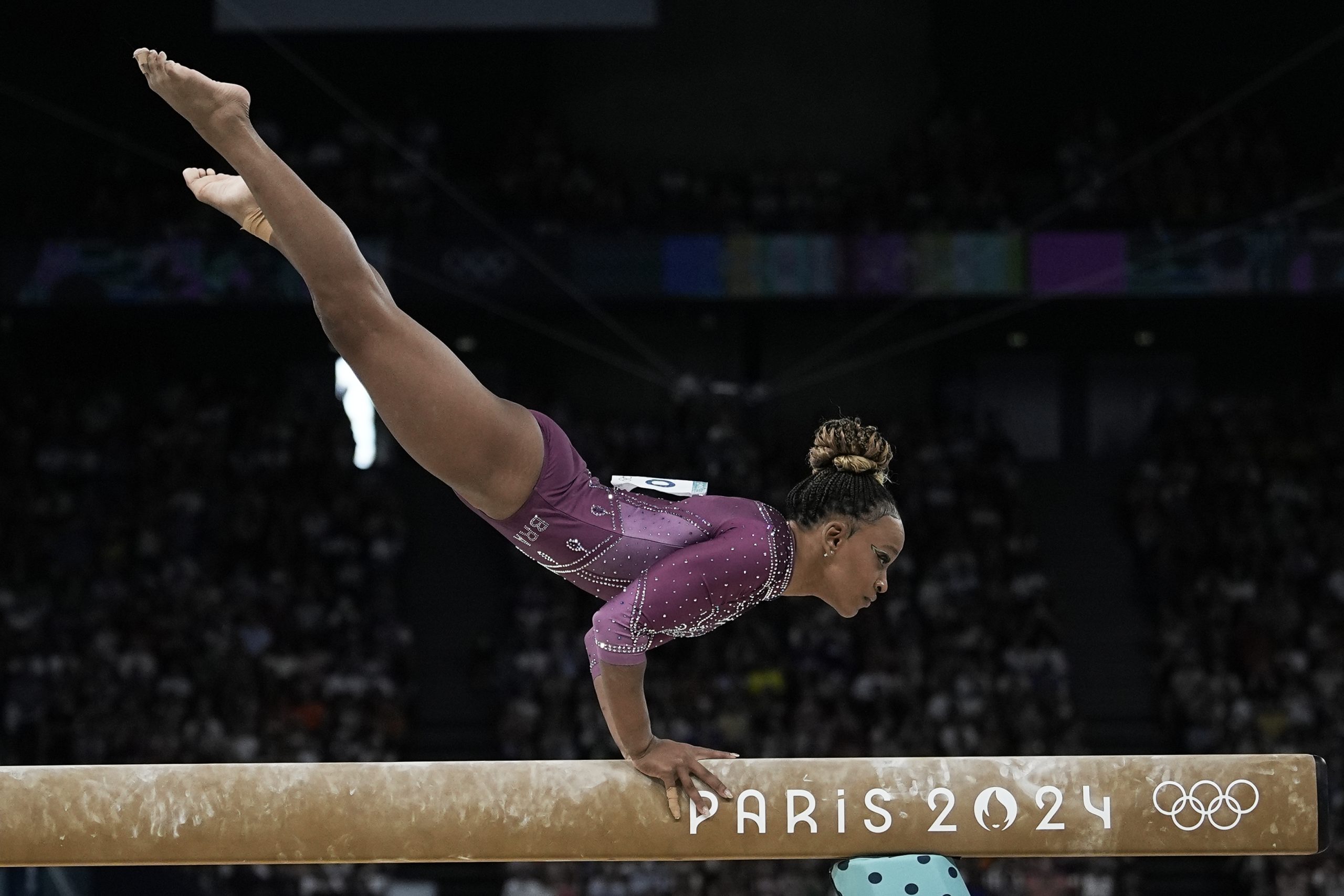 Ginasta brasileira realiza equilíbrio invertido na trave de equilíbrio com 'PARIS 2024' e Anéis Olímpicos.
