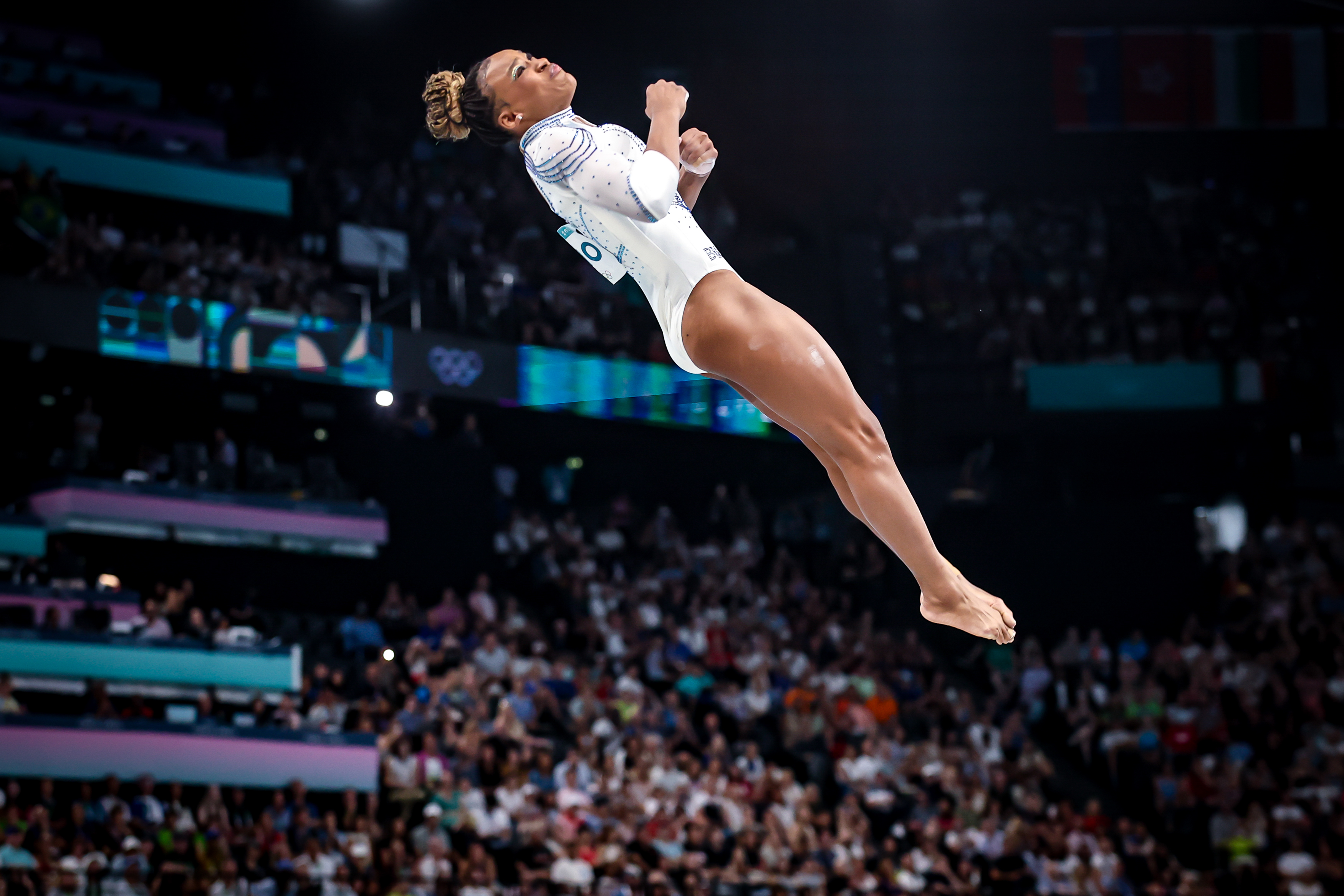 Ginasta de ponta-cabeça no ar, realizando salto acrobático em competição com público.