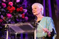 Judi Dench, de cabelos brancos, discursa em púlpito com microfone.
