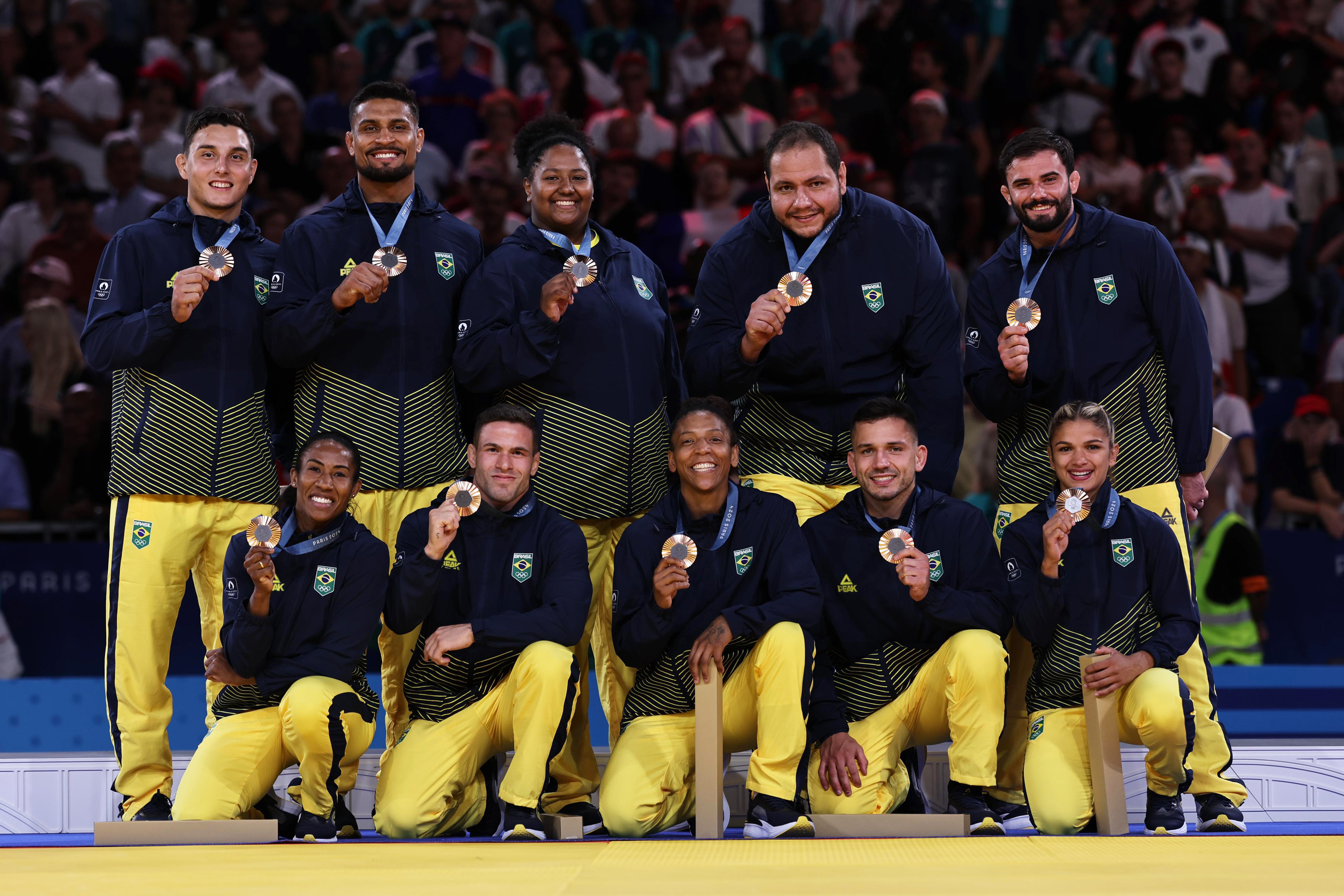 Atletas brasileiros sorridentes em uniformes azuis e amarelos exibindo suas medalhas de bronze.