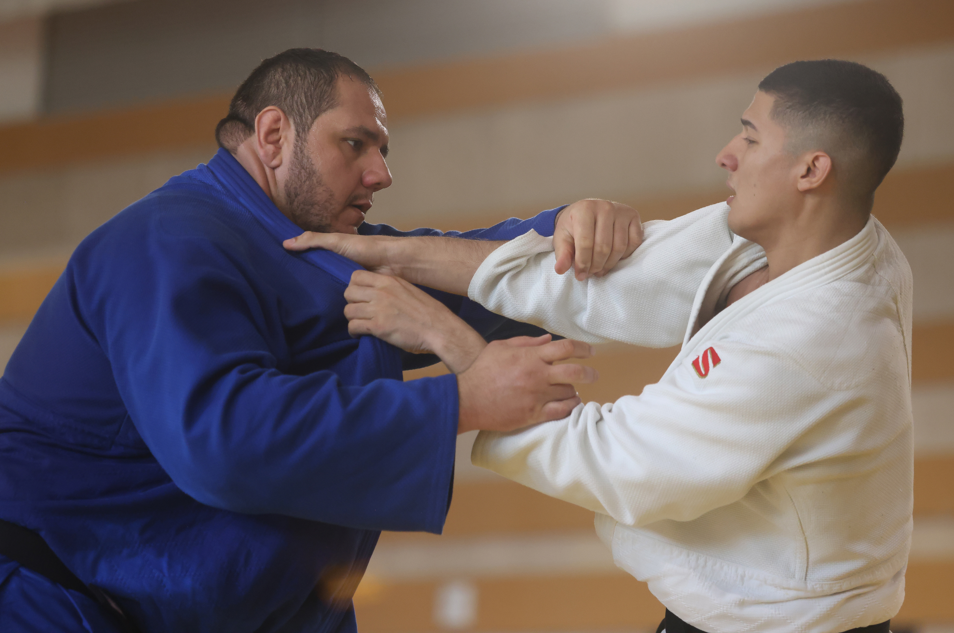 Dois judocas, um de kimono azul e outro branco, treinando judô.