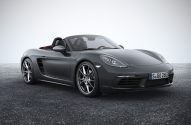 Carro esportivo Porsche Boxster cinza conversível, estacionado sobre asfalto em fundo claro.