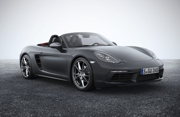 Carro esportivo Porsche Boxster cinza conversível, estacionado sobre asfalto em fundo claro.