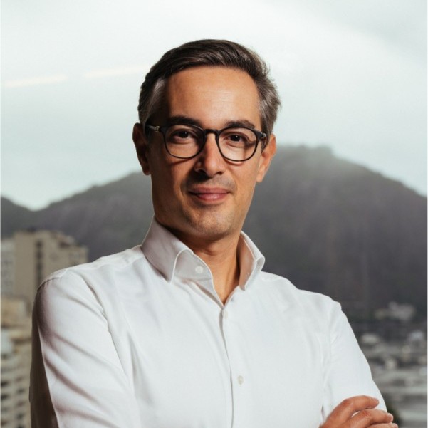 Homem de óculos, camisa branca, braços cruzados, olhando para a câmera com um sorriso.