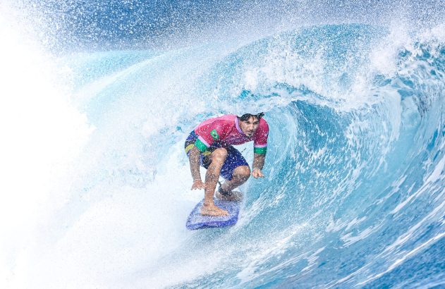 Bodyboarder em camisa rosa surfando dentro de um tubo de onda azul, com spray de água.