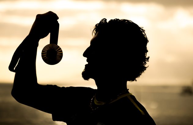 Silhueta de homem segurando e admirando uma medalha contra a luz do sol.