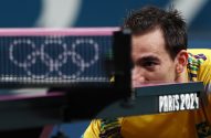 Atleta de tênis de mesa brasileiro focado, olhando a rede. Anéis olímpicos e 'Paris 2024' em destaque.