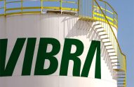 Tanque industrial branco com logo VIBRA verde. Escada espiral amarela e pássaro no topo da estrutura.