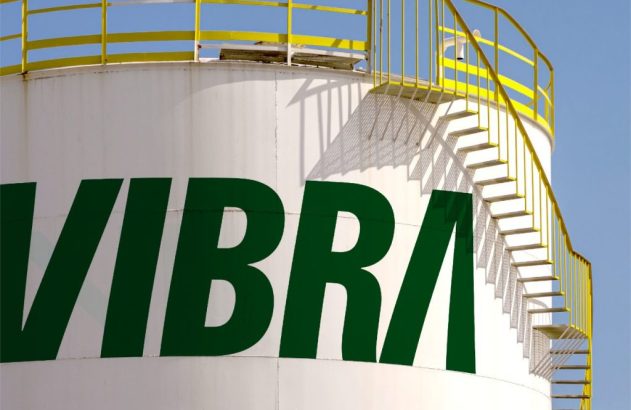 Tanque industrial branco com logo VIBRA verde. Escada espiral amarela e pássaro no topo da estrutura.