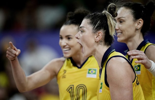 Três jogadoras de vôlei do Brasil em amarelo. Uma grita, outra aponta e sorri.