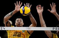 Jogador de vôlei de camisa amarela nº 28 bloqueia a bola sobre a rede, com outros dois bloqueadores ao lado.