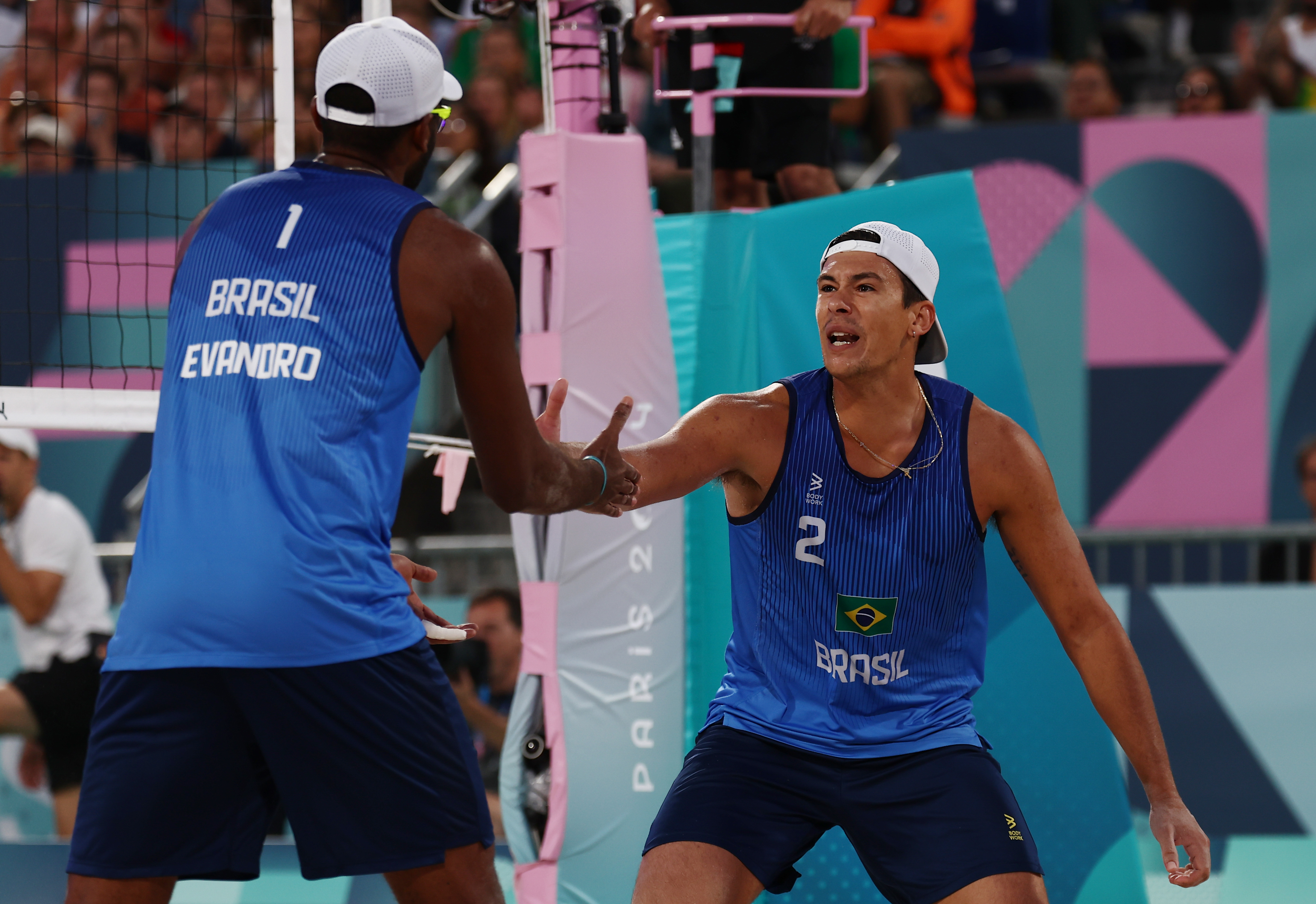Dois jogadores de vôlei de praia do Brasil se cumprimentam sobre a rede. Evandro (nº 1, de costas) e o jogador nº 2.