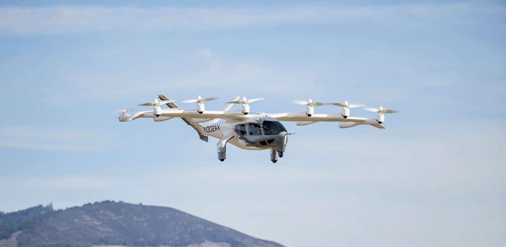 Aeronave eVTOL branca voando em céu azul sobre montanhas.