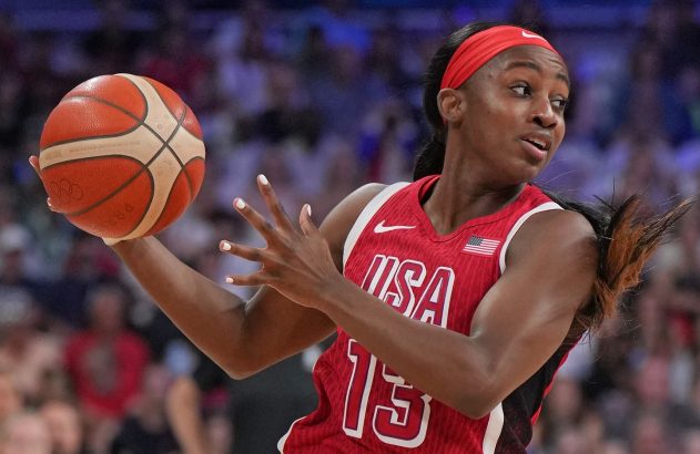 Jogadora de basquete feminina dos EUA, camisa 15, segurando uma bola olímpica, com olhar focado.