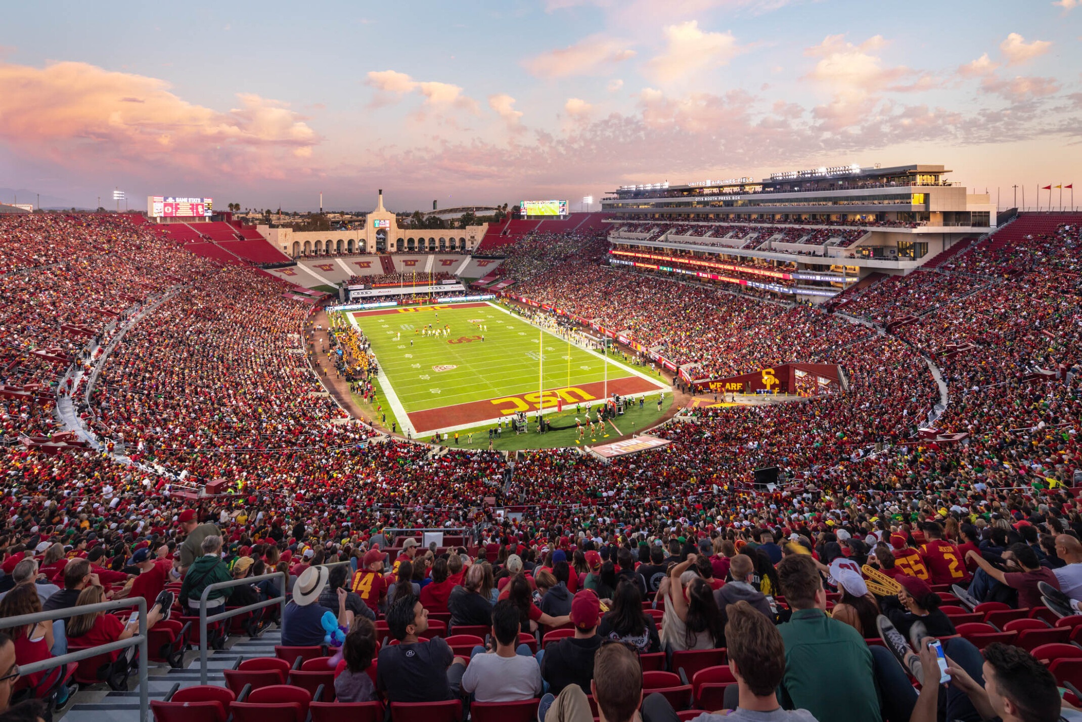 Estádio lotado de futebol com multidão em vermelho e campo verde exibindo 'USC' ao entardecer.