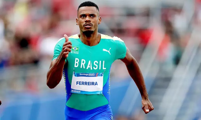 Atleta brasileiro Ferreira corre na pista em uniforme verde e azul.