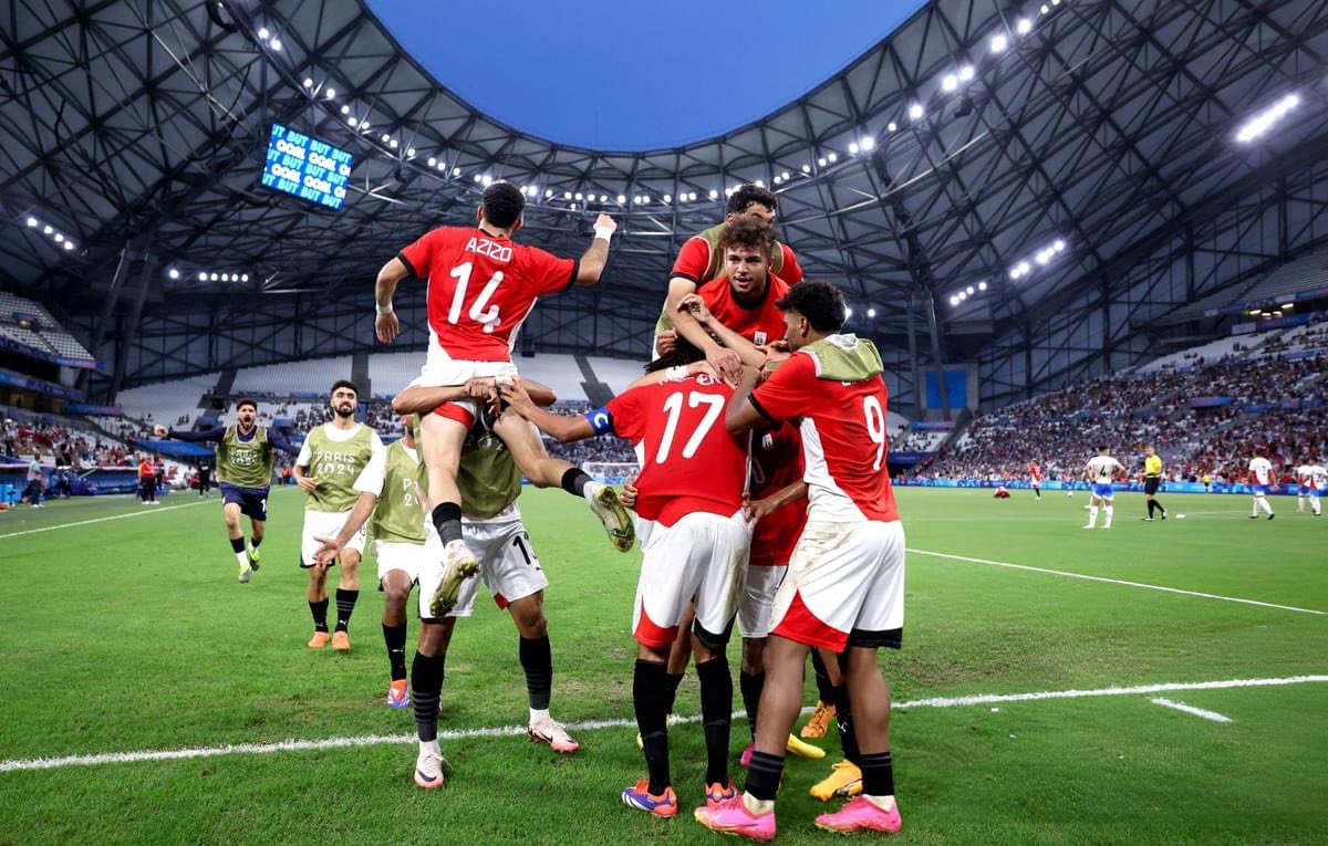 Time em uniformes vermelhos celebra em grupo no gramado de estádio.