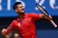 Novak Djokovic, tenista de camisa vermelha, expressa esforço intenso em quadra, com raquete e punho cerrado.