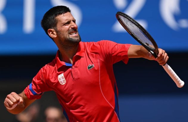 Novak Djokovic, tenista de camisa vermelha, expressa esforço intenso em quadra, com raquete e punho cerrado.