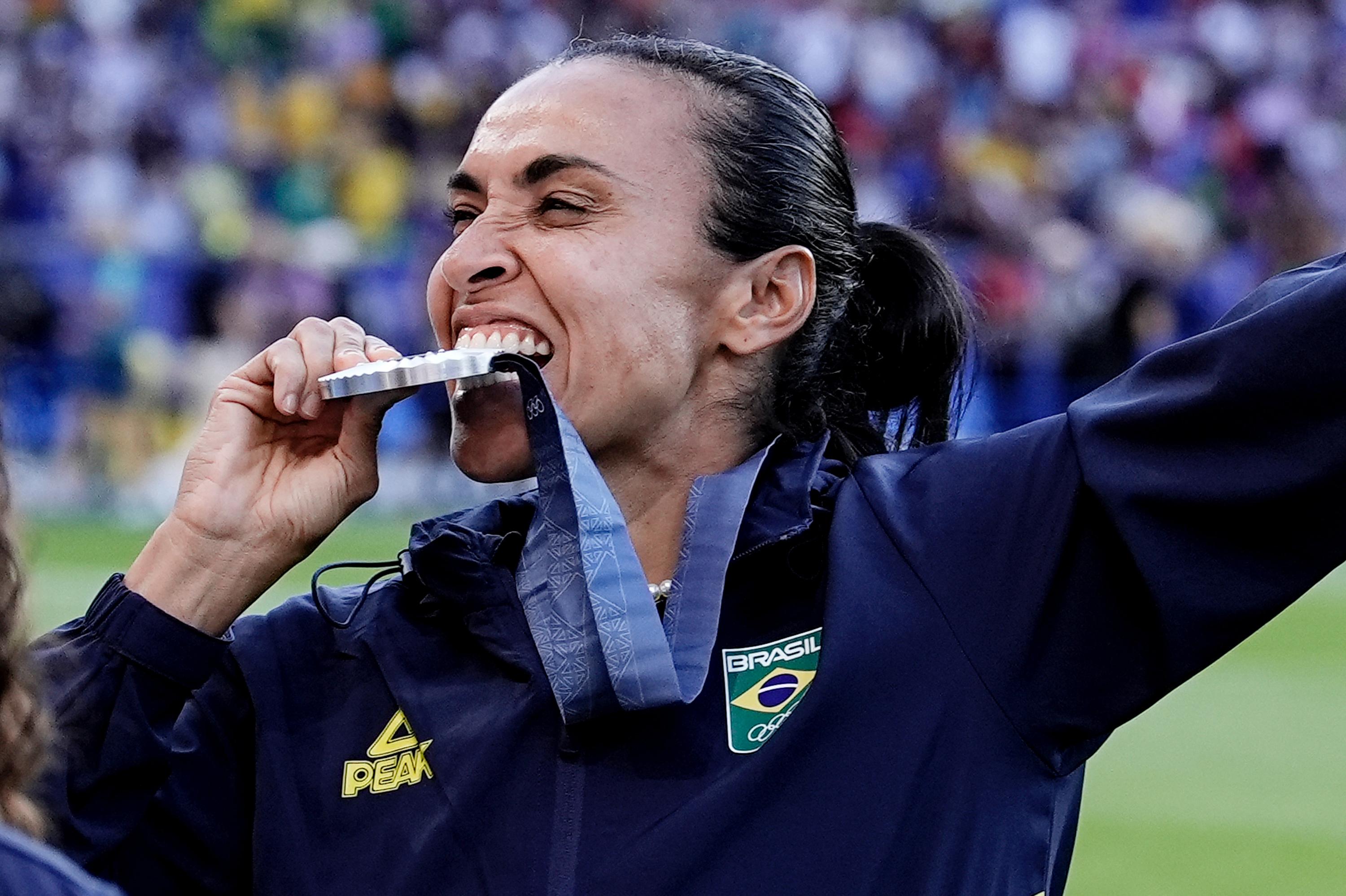 Mulher atleta sorrindo, morde medalha no pescoço durante celebração.