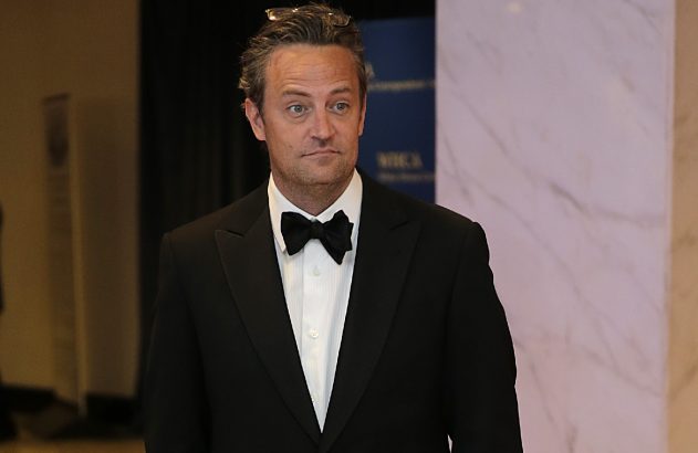 Matthew Perry de terno preto e gravata borboleta, olhando para a direita em ambiente formal.