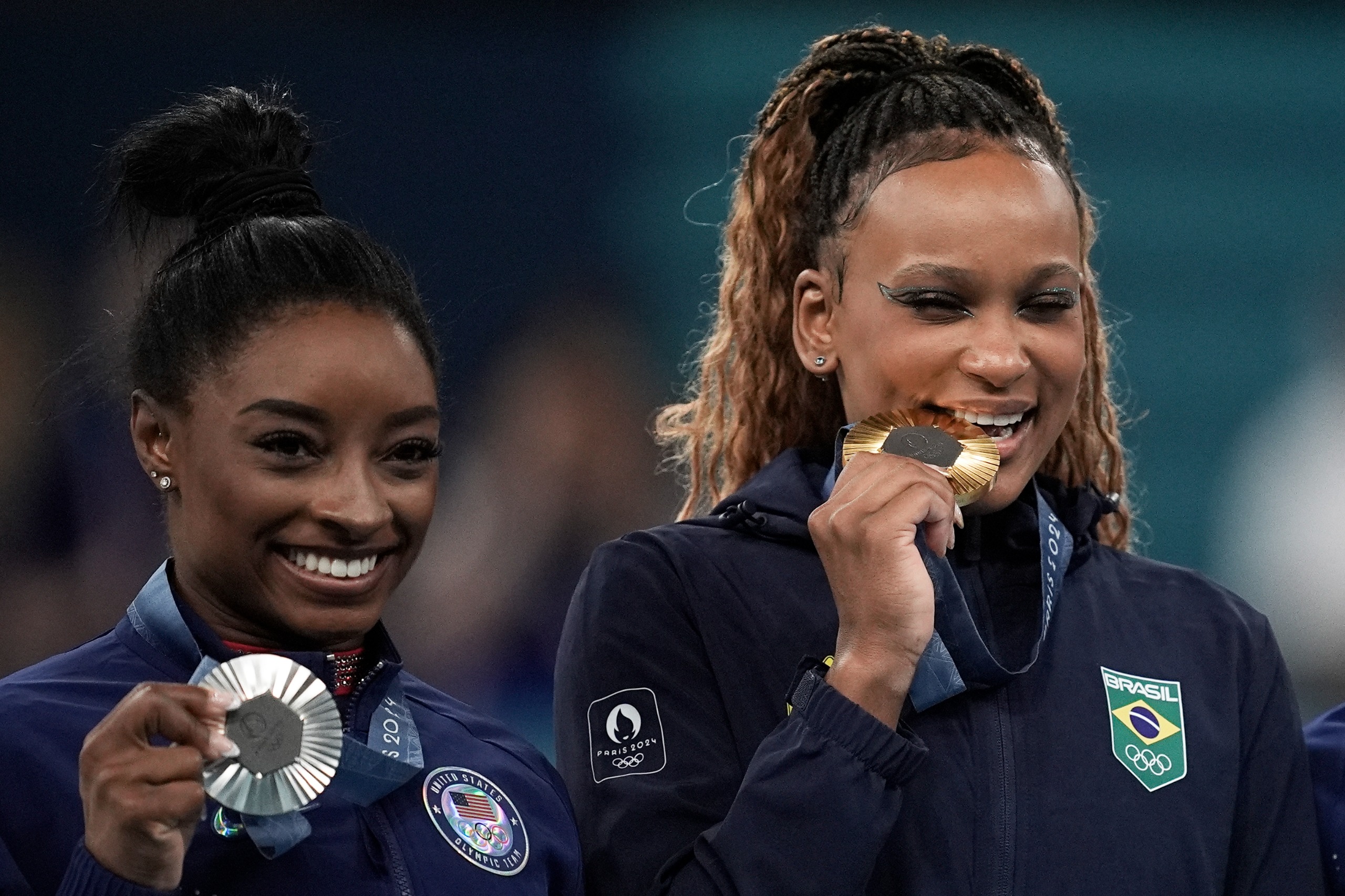 Simone Biles com prata e Rebeca Andrade mordendo ouro, ambas sorrindo.