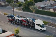 Tesla Semi branco transporta vários veículos Tesla, incluindo um Cybertruck, em cegonha por uma rua.