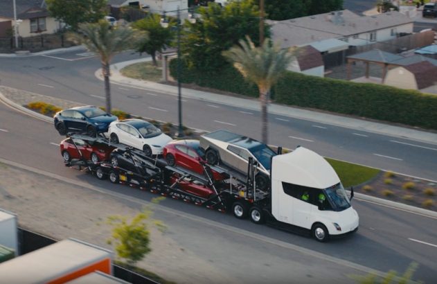 Tesla Semi branco transporta vários veículos Tesla, incluindo um Cybertruck, em cegonha por uma rua.