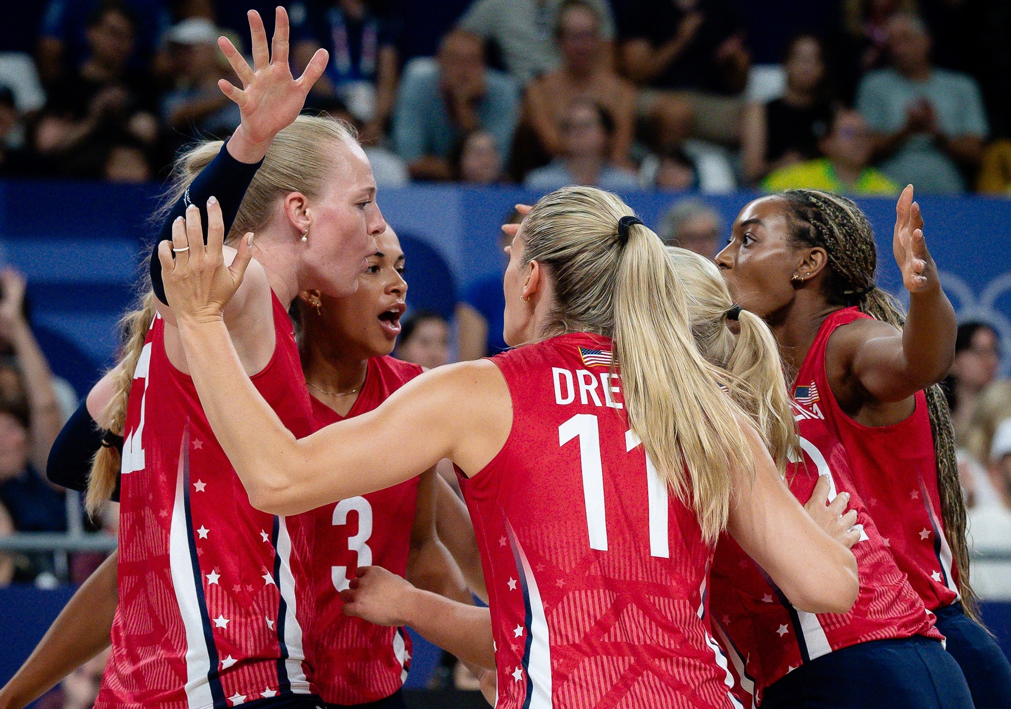 Jogadoras da seleção de vôlei feminino dos EUA em uniformes vermelhos celebram juntas em quadra.