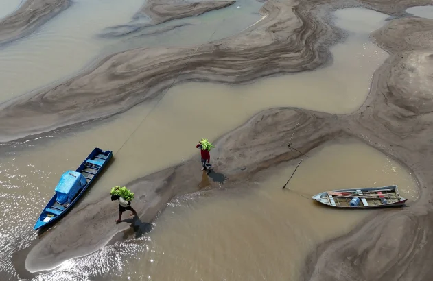 Pessoas carregam bananas caminhando sobre bancos de areia em meio à seca que afeta o Rio Solimões no Amazonas
