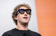 Mark Zuckerberg tem cabelos loiros encaracolados, está de óculos escuros e camiseta preta