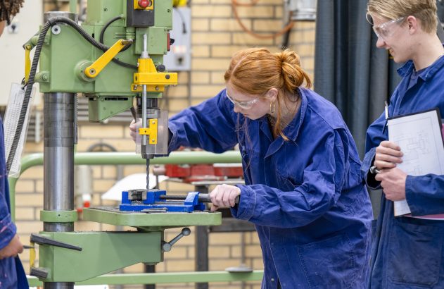 Duas pessoas em macacão azul trabalhando em uma máquina industrial