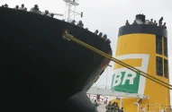 Recorte de um navio petroleiro com trabalhadores na borda do convés, observando o porto. Em segundo plano, uma chaminé amarela com o logo da BR distribuidora.