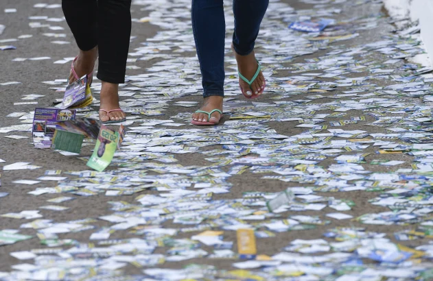 Pessoas andando em calçada cheia de santinhos de candidatos em frente a seção eleitoral