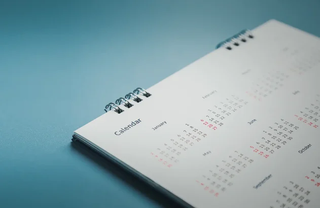 Um calendário de mesa espiral minimalista deitado sobre uma superfície plana com fundo azul.