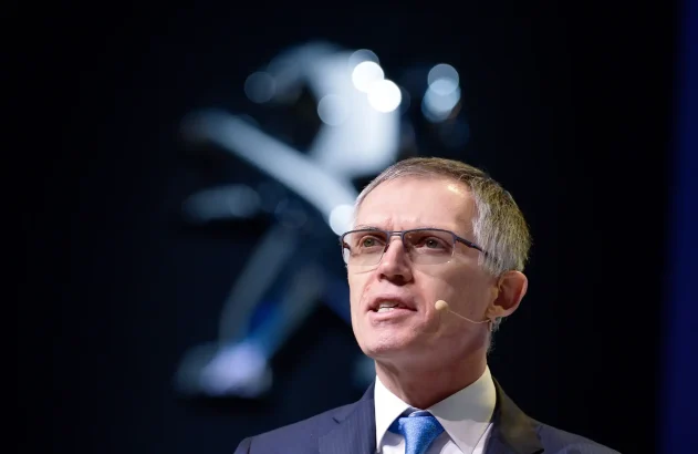 Foto de busto de Carlos Tavares, CEO da Stellantis, multinacional fabricante de automóveis. Ele é um homem branco, grisalho, de cabelos curtos; usa óculos e um terno cinza com gravata azul claro.