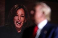 Kamala Harris sorri em tela, Donald Trump desfocado em primeiro plano, olhando.