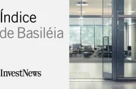 Na imagem apresentada, à esquerda, temos "Índice de Basileia" em letras grandes e estilizadas sobre fundo branco com a logomarca "InvestNews" abaixo; à direita, uma fotografia de um ambiente corporativo moderno e iluminado, com mesas, cadeiras e computadores visíveis através de portas de vidro.