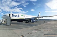 A imagem mostra um avião da companhia aérea Azul estacionado na pista de um aeroporto em um dia claro, com céu azul e algumas nuvens.