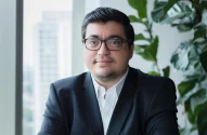O economista Felipe Salto, um homem de cabelo curto e escuro, usando terno preto e óculos, está em um escritório com janela grande e uma planta verde ao fundo.
