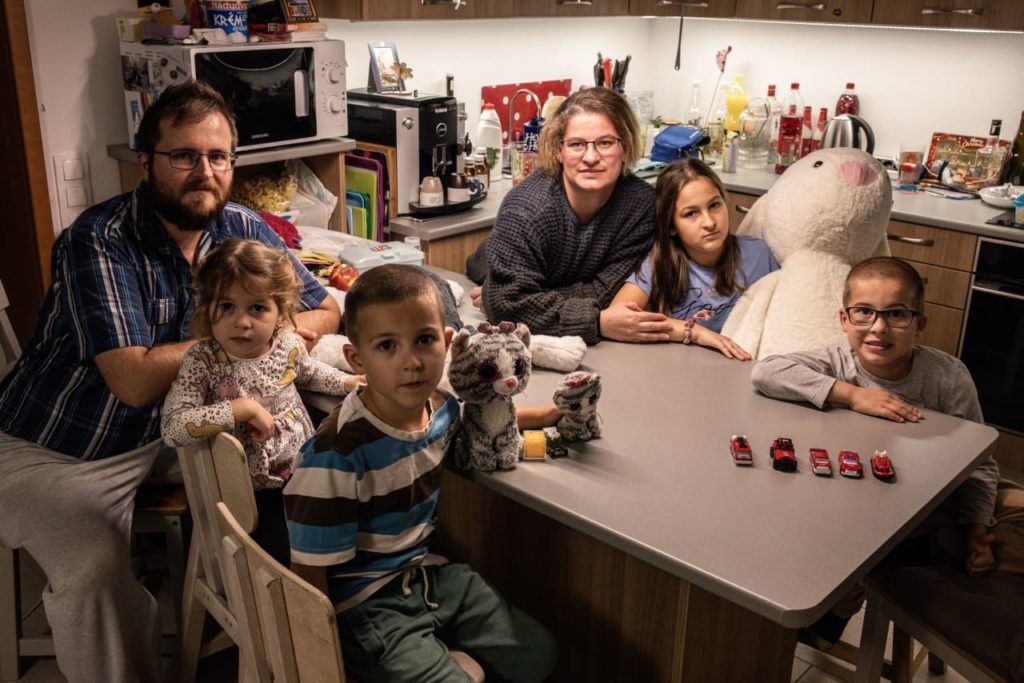 Família posando na cozinha: adultos e crianças, alguns sentados à mesa, outros de pé.